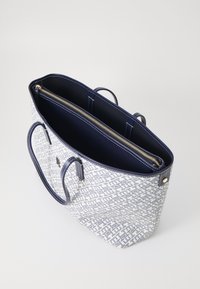 Borsa tote strutturata con un motivo geometrico blu e bianco, doppio manico e tasca interna con zip accentuata da hardware dorato.
