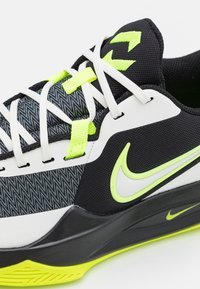Chaussure de sport Nike noire et blanche avec des accents jaune néon, des lacets blancs et un tissu texturé sur le dessus près de la semelle intermédiaire.