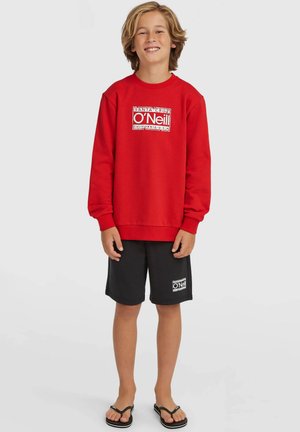 Rød sweatshirt med ribstrikkede ærmeender og kant, med et hvidt logotryk. Kombineret med sorte shorts og klipklappere. Afslappet sommeroutfit.