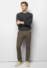 Donkergrijze lange mouwen crewneck trui, bruine slim-fit broek en beige sneakers. Gladde stof met subtiele textuur en getailleerd ontwerp.