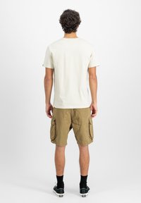 Helebees värvi lühikeste varrukatega t-särk ja khaki värvi cargo lühikesed püksid suurte taskutega, vaadatuna seljapoolt, ühtlase valge tausta ees.