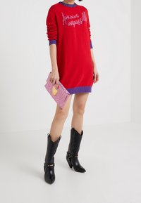 Red knitted sweater dress with purple cuffs, featuring "Amuse Impossil" text. Paired with pink textured clutch and tall black heeled boots.