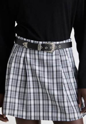 Jupe à carreaux noirs avec plis, en tissu léger, accompagnée d'une ceinture en cuir noir avec une boucle en argent ornée.