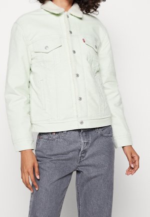 Personne portant une veste en jean claire doublée sherpa avec des boutons sur le devant et un jean gris taille haute.