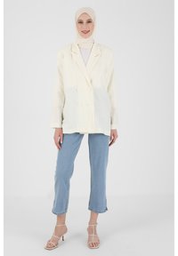 Cream double-breasted blazer with textured fabric, two front buttons, paired with light blue cropped jeans and strappy beige heels.