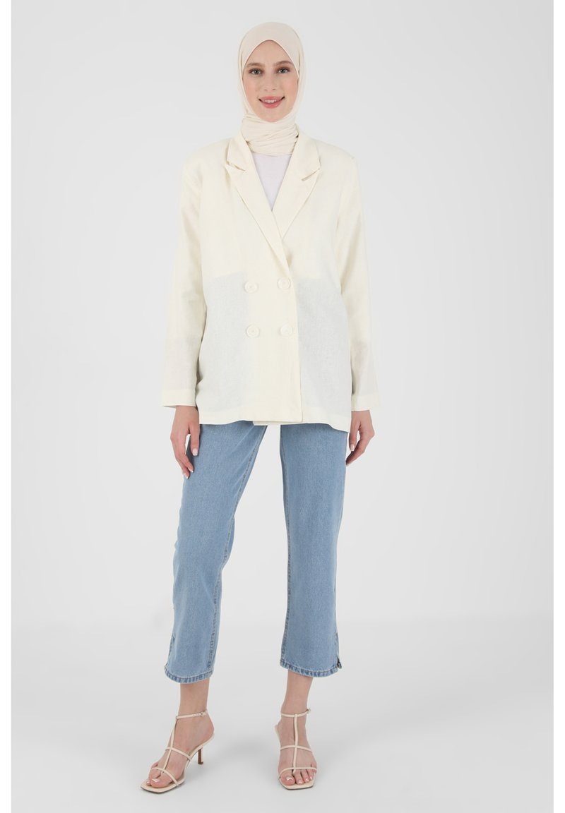 Cream double-breasted blazer with textured fabric, two front buttons, paired with light blue cropped jeans and strappy beige heels.