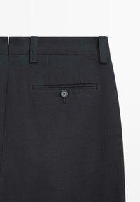 Pantaloni neri da donna con passanti per cintura e una tasca posteriore con bottone a filetto su sfondo semplice.