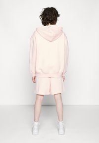 Sudadera de color rosa claro con capucha y puños acanalados, combinada con pantalones cortos a juego. Ambas piezas tienen una textura suave y un corte relajado.