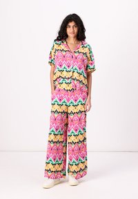 Completo colorato a due pezzi composto da una maglietta a maniche corte e pantaloni a gamba larga con un motivo geometrico nei colori rosa, giallo, verde e nero.