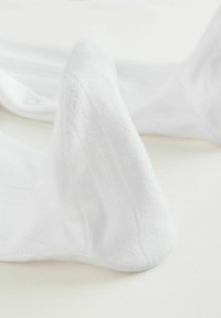 Weiße Baumwollsocken mit strukturierten Mustern, die gerippte Abschnitte und eine glatte Oberfläche aufweisen. Nahaufnahme zeigt den Zehenbereich.