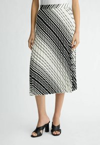Falda plisada de longitud media con un patr�ón de rayas diagonales en blanco y negro. La cintura también tiene rayas; combinada con mules de tacón cuadrado negros.
