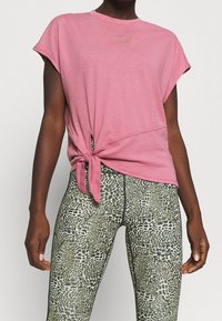Rosa t-shirt med kort ärm och knutdetalj i sidan, med en liten präglad logotyp, kombinerad med högmidjade leggings i ett grönt djurmönster.