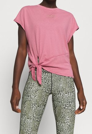 Camiseta rosa de manga corta con detalle de nudo lateral, que presenta un pequeño logo en relieve, combinada con leggings de cintura alta en un estampado de animal verde.