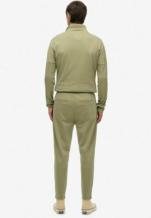 Grøn sweatshirt og matchende joggers med en blød tekstur. Har en høj krave og baglommer, båret med lyse sko.