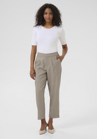 Haut léger en blanc à nervures associé à un pantalon beige ajusté à taille haute, avec des plis et des poches latérales. Talons aiguilles beiges.
