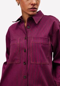 Fuchsia- und schwarze gestreifte Hemd-Bluse aus strukturiertem Stoff, mit zwei Brusttaschen und klassischem Kragen.