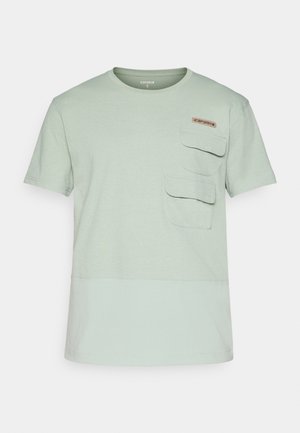 Helles grünes T-Shirt mit kurzen Ärmeln und rundem Ausschnitt, zwei vorderen Taschen und einem kleinen Logo-Patch auf der Brust. Weiches Textilmaterial.