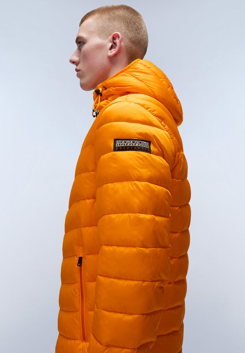 Chaqueta de plumas en un brillante color naranja, con un bolsillo con cremallera, capucha ajustable y un parche con el logo en la manga. Diseño acolchado con textura suave.