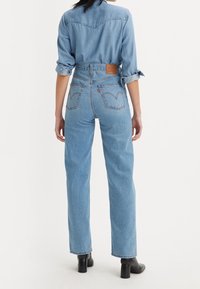 Vaqueros de mezclilla azul claro con un corte relajado, cintura alta y dos bolsillos traseros con un diseño sutil bordado. Botines negros puestos.