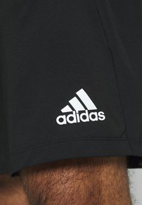 Musta urheilushortsit, joissa on sileä pinta ja joustovartinen vyöt ärö. Vasemmassa alakulmassa on valkoinen Adidas-logo.