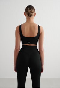Schwarzer, gerippter Sport-BH mit breiten Trägern und tiefem Rücken, kombiniert mit hochgeschnittenen, schwarzen, gerippten Leggings mit strukturiertem Nahtdetail.