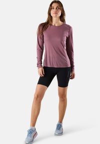 Pitkähihainen, luumuinen urheilupaita, jossa on sileä pinta; yhdistetty mustiin shortseihin ja vaaleansinisiin tennareihin, joissa on verkkokuviointi ja nauhat.