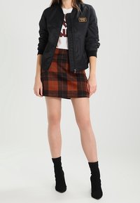 Giubbotto bomber nero con logo Vans, abbinato a una mini gonna a quadri marrone e arancione e stivaletti neri. Tessuto morbido e design aderente.
