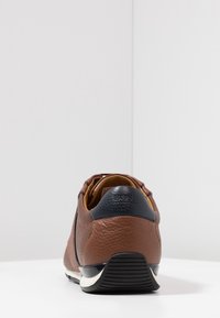 Baskets en cuir marron avec une finition texturée, talon bleu marine contrastant et semelle blanche. Présente un bout arrondi et un branding subtil à l'arrière.