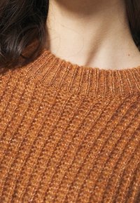 Rostfärgad stickad tröja med ribbad struktur och rund halsringning. Tyget ser mjukt och något ludet ut.
