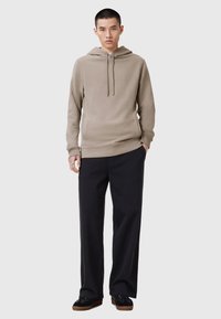 Sudadera con capucha beige con cordón, bolsillo frontal y puños acanalados. Combinada con pantalones de pierna ancha negros y zapatillas negras con suelas marrones.