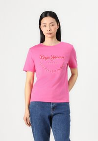 Rosa bomullströja med texten "Pepe Jeans London" och "Let's Get Lost in Music" i en kontrasterande stil. Kortärmad och rundad hals.