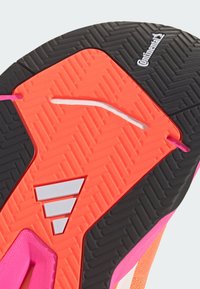 Die Schuhsohle besteht aus schwarzem strukturiertem Gummi, einer rosa Zwischensohle mit Fischgrätenmuster und einem leuchtend orangefarbenen Akzent mit weißen Branding-Elementen und Details.