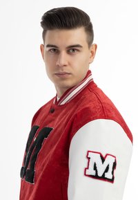 Giacca varsity rossa in tessuto testurizzato, lettera "M" in feltro nero sul petto, maniche in pelle bianca e colletto e polsini a coste a righe.