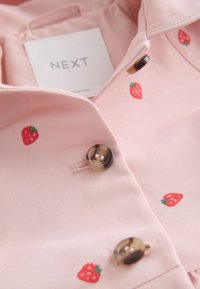 Chemise rose clair avec de petites fraises rouges brodées, des boutons marron et une étiquette blanche indiquant NEXT à l'intérieur du col.