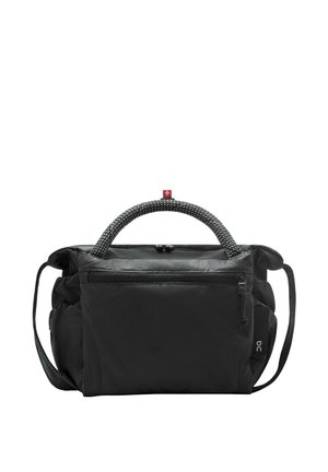 Vrouw met gevlochten haar, gekleed in een beige mouwloze romper met ritssluiting, een zwarte crossbodytas, witte sokken en beige sneakers, staand en naar voren gekeerd.