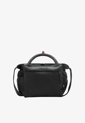 Vrouw met gevlochten haar, gekleed in een beige mouwloze romper met ritssluiting, een zwarte crossbodytas, witte sokken en beige sneakers, staand en naar voren gekeerd.