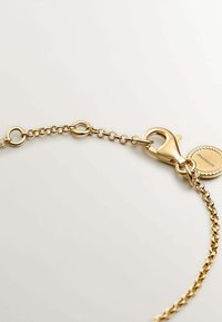 Pulsera de cadena de oro con un cierre de langosta, que presenta eslabones ovalados y un charm redondo con un patrón de cuerda. Acabado suave y pulido.