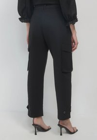 Schwarze Cargo-Hosen mit lockerer Passform, Seitentaschen und Knöpfen an den Bündchen. Glatte Textur und ein Bund mit elastischen Details.