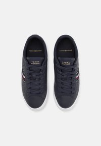 Sötétkék sportcipő sima bőr felső résszel, fehér talppal és arany logóval. Jellemzője a színes csíkok az oldalon és a standard fűződizájn.