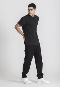 Svart t-shirt med kort ärm och rundad halsringning, kombinerad med svarta byxor och vita sneakers. Enkelt mönster med minimala detaljer.