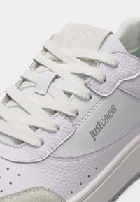 Λευκό αθλητικό παπούτσι Just Cavalli με υφή δέρματος, λευκά κορδόνια και λογότυπο στη πλευρά, με επενδυμένο περιμετρικά κολάρο και οπές για εξαερισμό.