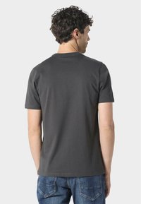 Szürke, rövid ujjú póló, sima pamutból készült, kerek nyakkal és enyhe rugalmassággal. A hátsó nézet tiszta kidolgozást mutat díszítések nélkül.