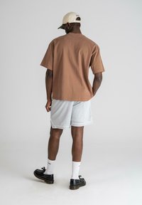 Brown short-sleeve shirt, paired with gray mesh shorts. Black shoes and white socks. The background is gray, enhancing the outfit's colors.