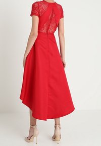 Röd klänning med korta spetsärmar, hög-låg fåll. Har en dragkedja i ryggen och spetsdetaljer på bodice. Bärs med nakna klackar.