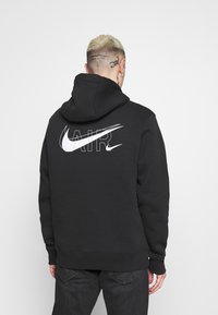 Černá mikina s kapucí s velkým bílým logem "AIR" a logem Nike na zadní straně. Obsahuje kapuci a žebrované manžety, vyrobena z měkkého materiálu.
