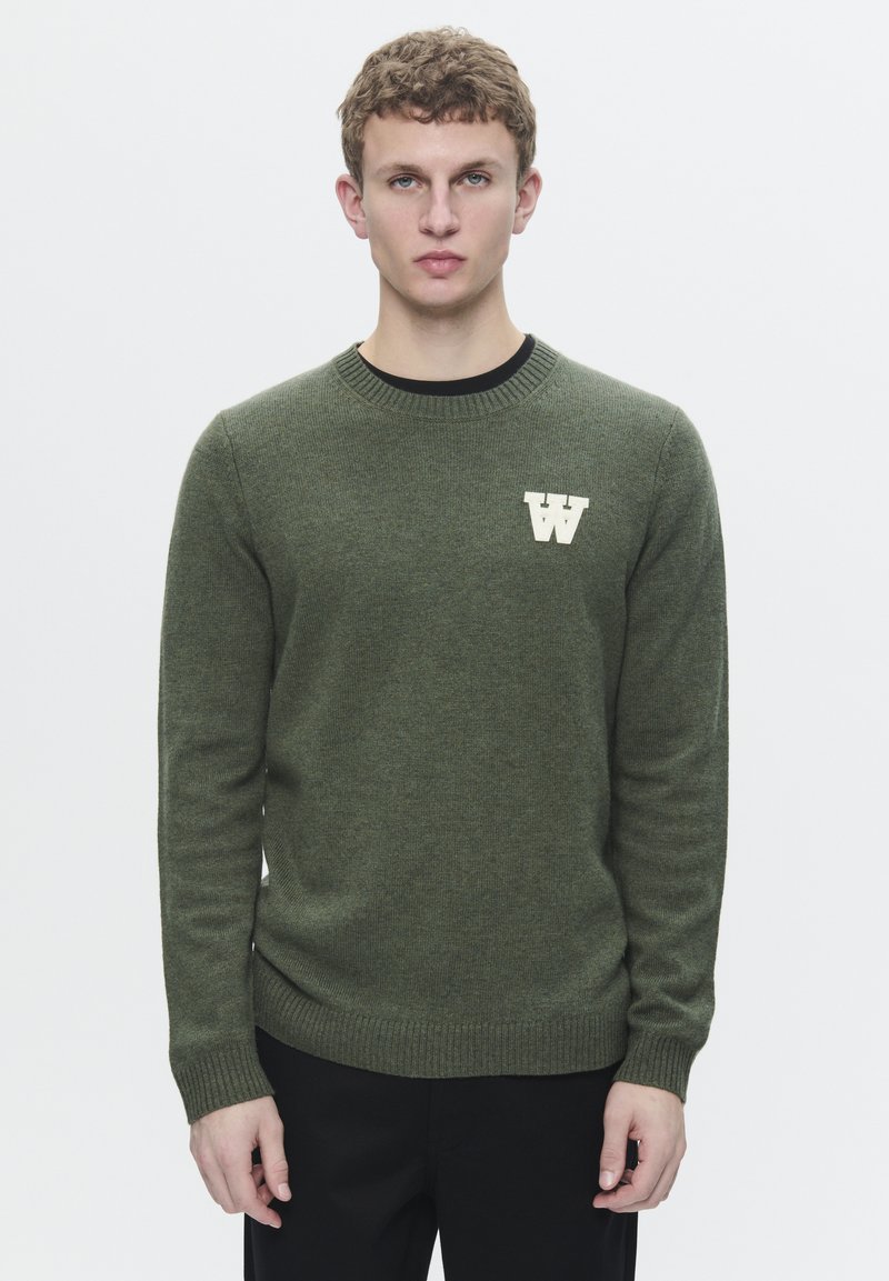 Olivgrüner Pullover mit Rundhalsausschnitt und gerippten Bündchen, ausgestattet mit einem weißen 'W'-Logo auf der Brust, aus einem strukturierten Strickstoff gefertigt.