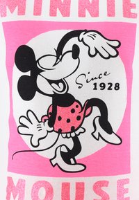 Grafika Minnie Mouse na białym materiale. Charakteryzuje się czarno-różowym wzorem w kropki oraz błyszczącym tekstem. Tekst brzmi: "Minnie Mouse od 1928 roku."