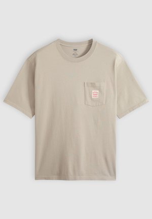 Beige katoenen T-shirt met korte mouwen en een borstzakje met een klein rood-wit label, getoond tegen een effen achtergrond.