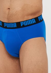 Modré bavlnené slipy s čiernym pásom, na ktorom je modrý text "PUMA". Hladká textúra, priliehavý strih, ktorý zdôrazňuje pohodlie a podporu.