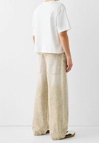 Vit t-shirt i cropped-modell och ljusbeige jeans med vida ben i denim med en urtvättad textur. Har två bakfickor och en avslappnad passform. Avslappnat fotarbete synligt.